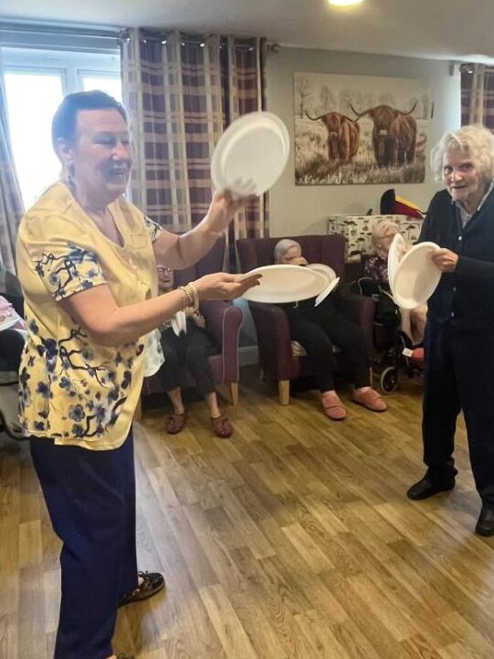resident and entertainer smiling and clapping paper plates together and dancing