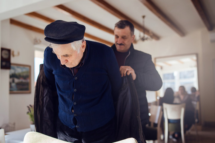 old man getting help putting his coat on