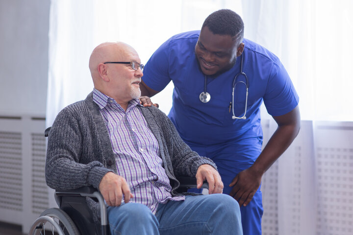 resident in wheelchair with nurse helping him a